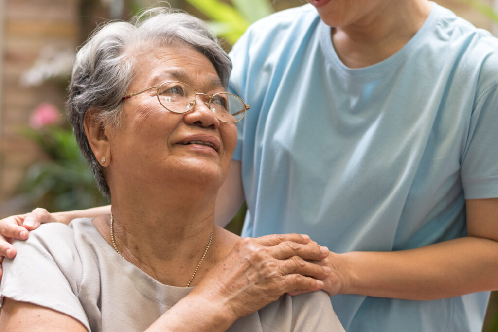 Caregiver resting hands on the shoulders of a smiling elderly woman outdoors