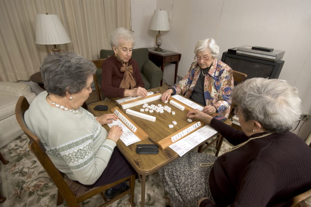 Four senior women playing a tile game together around a living room table